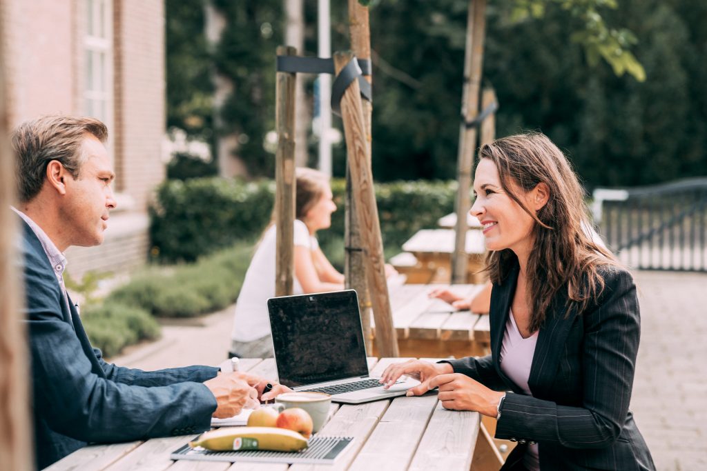 Twee personen aan een picknicktafel met laptop en fruit