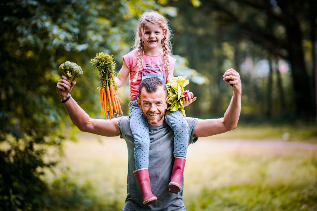 Man met meisje op zijn schouders samen laten ze groentes zien  